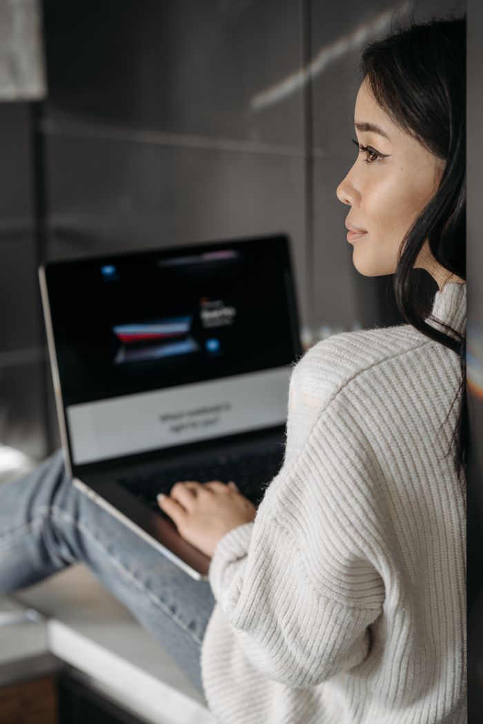 Asian woman in a cozy setting using a laptop, reflecting tech lifestyle.